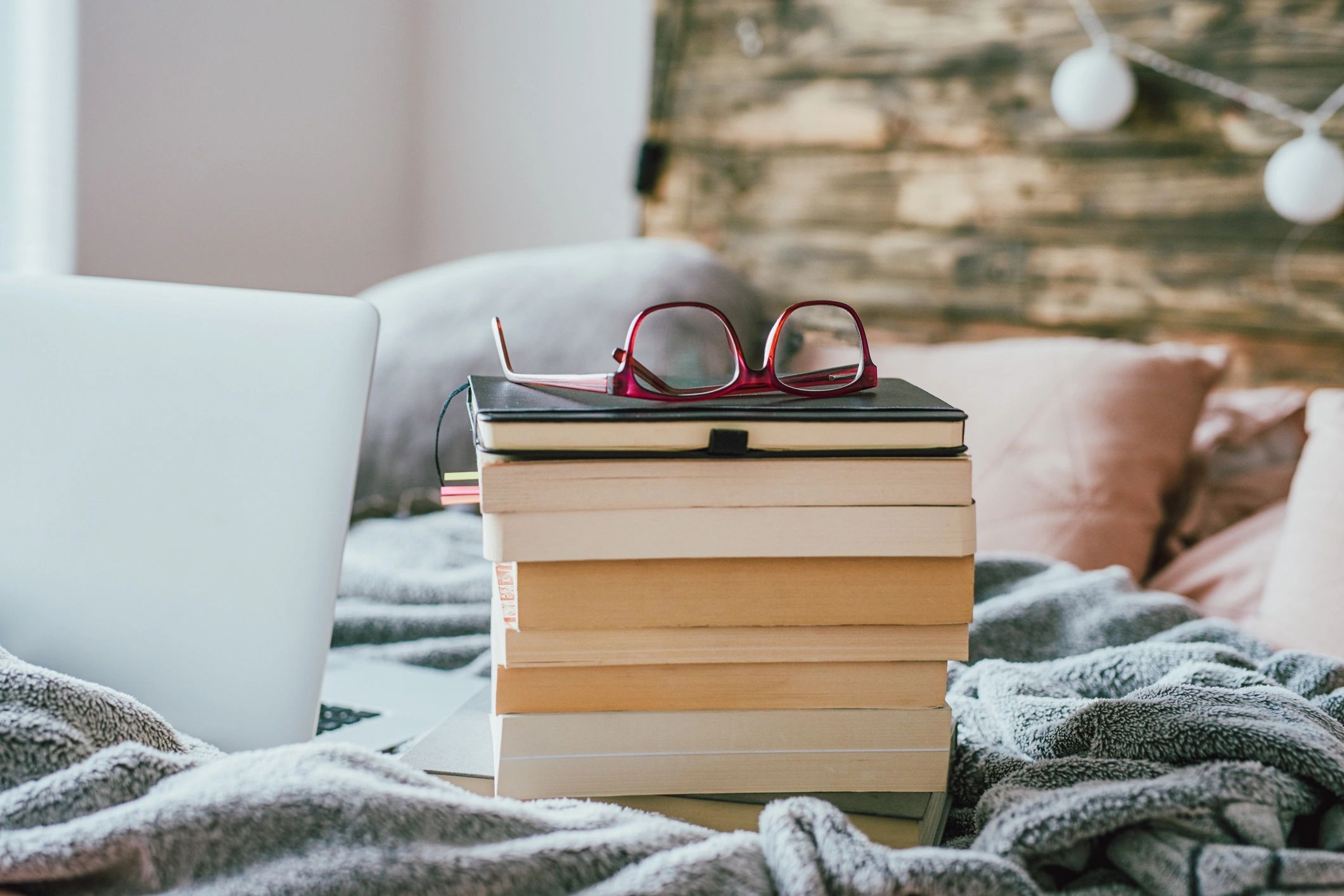 Stack of books on a bed next to a laptop